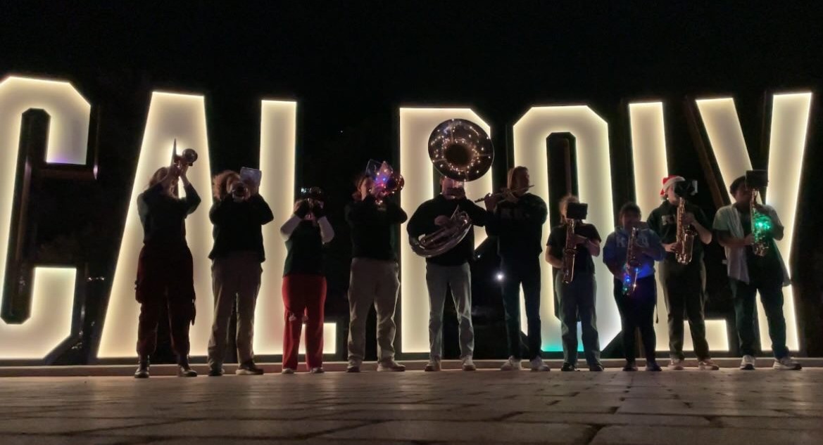 Brothers of Iota Pi playing Holiday music in front of the Cal Poly sign.